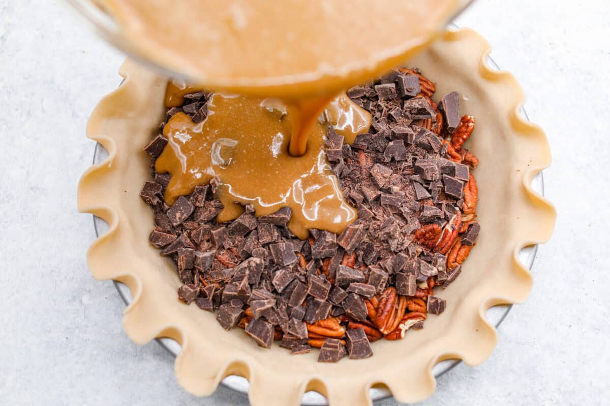 Chocolate pecan pie is a sweet, decadent dessert with a buttery crust filled with gooey caramel, crunchy pecans, and rich chocolate. It's the perfect pie to share this Thanksgiving. It will knock your family's socks off! Overhead shot of someone pouring the egg, sugar and butter mixture over the chocolate and pecans in the pie crust.