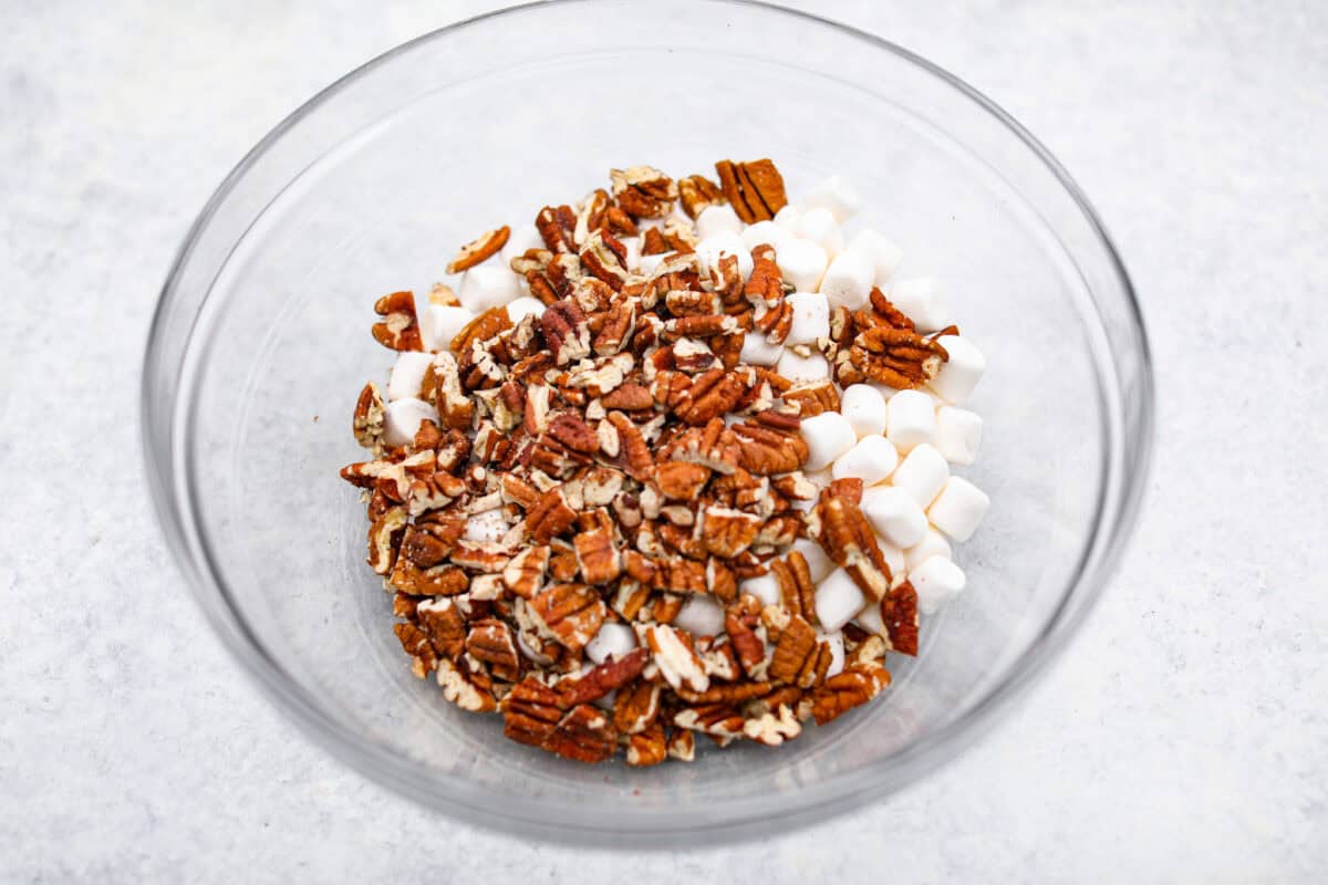 These decadent rocky road bars are the best no-bake treat that you can whip up in no time when that sweet tooth hits. Fudgy chocolate, soft marshmallows, and chewy pecans combine to make the most amazing dessert. Overhead shot of pecans with mini marshmallows in a glass bowl.