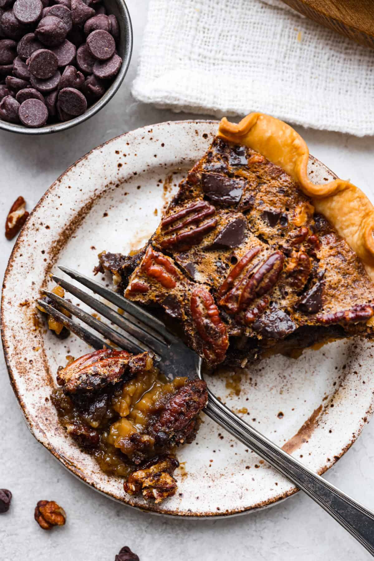 Chocolate pecan pie is a sweet, decadent dessert with a buttery crust filled with gooey caramel, crunchy pecans, and rich chocolate. It's the perfect pie to share this Thanksgiving. It will knock your family's socks off! Overhead shot of a plated slice of chocolate pecan pie.
