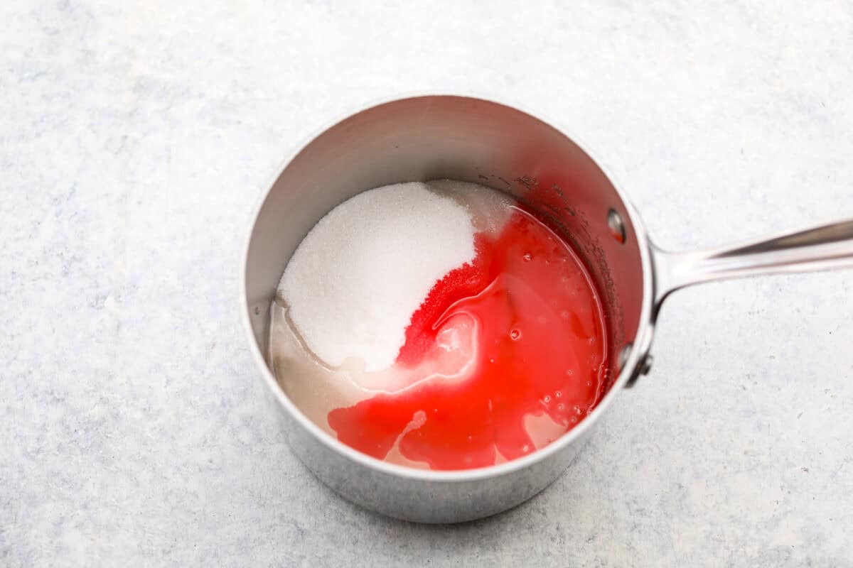 Homemade cherry cordials are a tasty, nostalgic treat! They're made with sweet cherries that are coated in a rich chocolate shell. Make them for Christmas or Valentine’s Day, and watch them disappear! Overhead shot of sugar, water corn syrup and maraschino liquid in a saucepan.