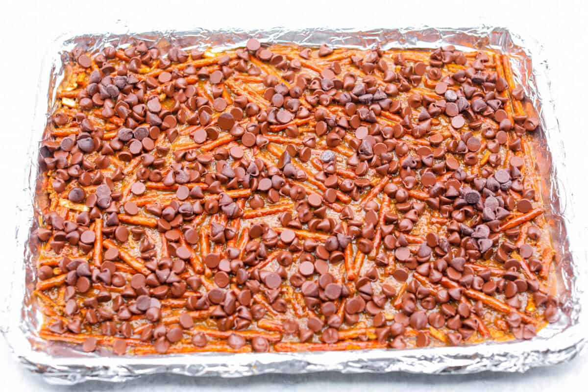 Pretzel Christmas Crack is the best holiday treat! This addictive combination of salty pretzels, rich toffee, and chocolate is sure to be a hit at any party or gathering. Overhead shot of chocolate chips sprinkled over baking sheet.
