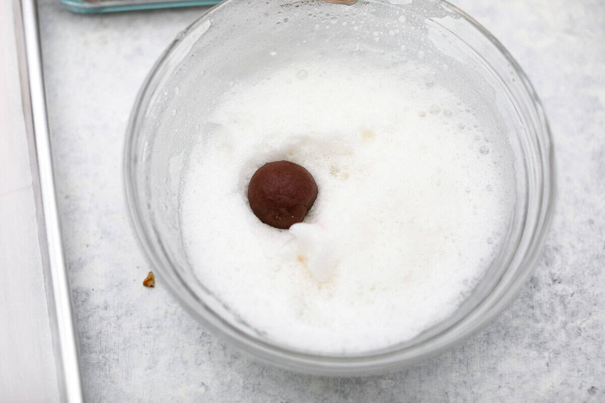 Turtle Cookies are a baked, bite-size brownie loaded with pecans, then filled with a creamy caramel center for a rich, decadent holiday cookie! These turtle cookies are always a huge hit and are gone in minutes Overhead shot of a turtle cookie dough ball in the bowl of whipped egg whites.