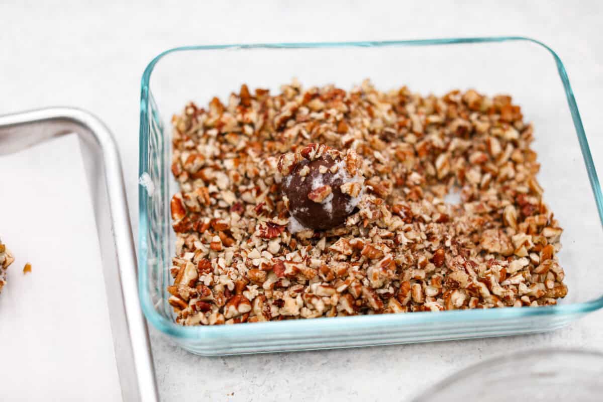 Turtle Cookies are a baked, bite-size brownie loaded with pecans, then filled with a creamy caramel center for a rich, decadent holiday cookie! These turtle cookies are always a huge hit and are gone in minutes Angle shot of egg white coated dough ball in chopped pecans.