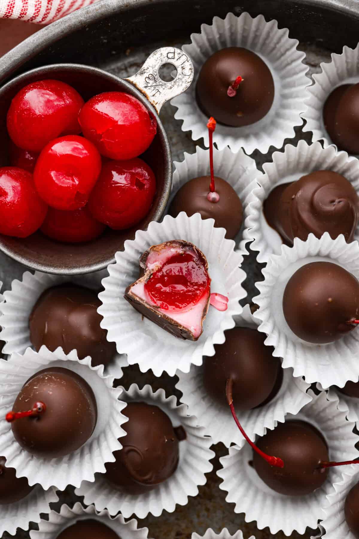 Homemade cherry cordials are a tasty, nostalgic treat! They're made with sweet cherries that are coated in a rich chocolate shell. Make them for Christmas or Valentine’s Day, and watch them disappear! Overhead shot of cherry cordials in paper wrappers with one that has a bite taken out.