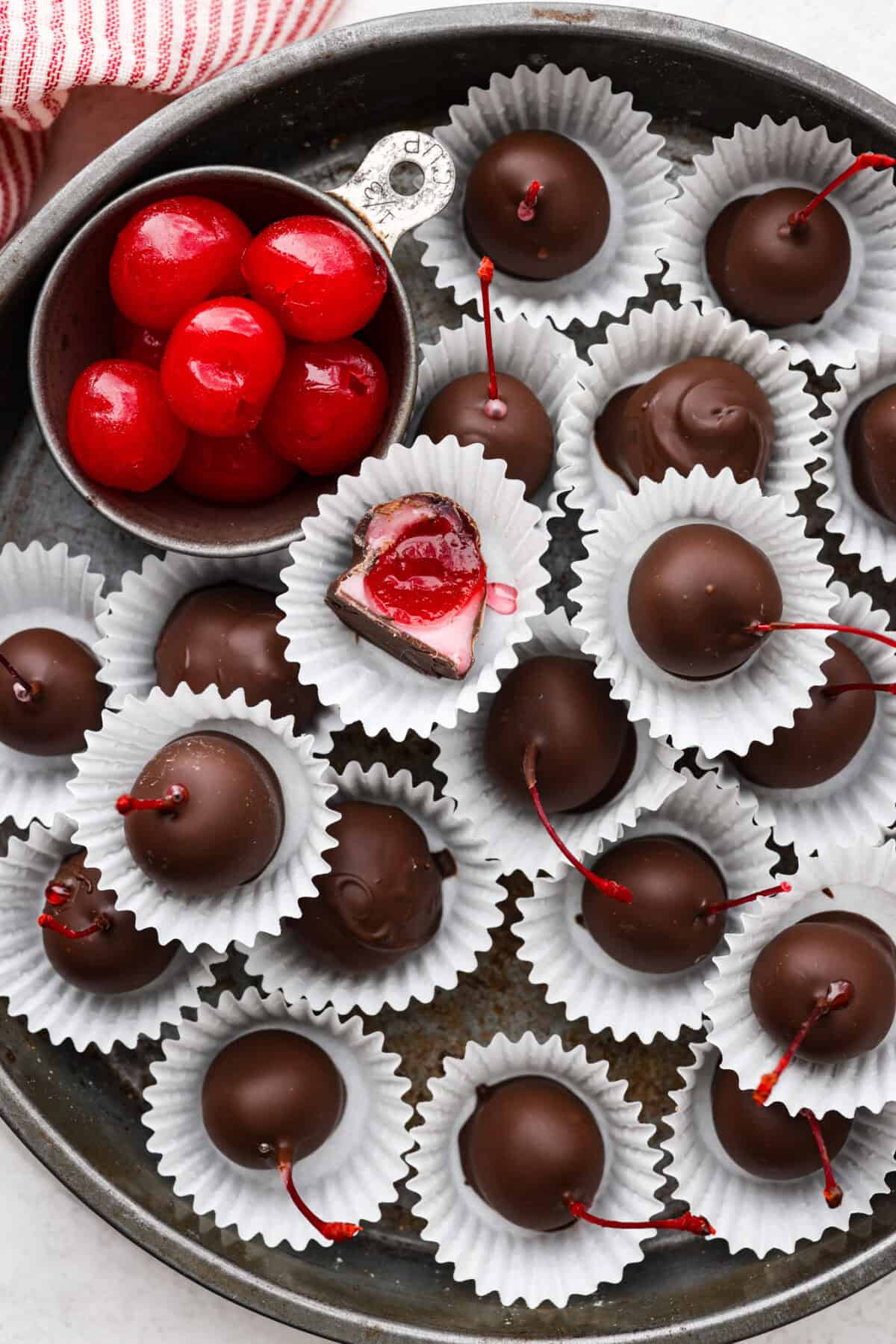 Homemade cherry cordials are a tasty, nostalgic treat! They're made with sweet cherries that are coated in a rich chocolate shell. Make them for Christmas or Valentine’s Day, and watch them disappear! Overhead shot of cherry cordials in paper wrapping on a serving platter.