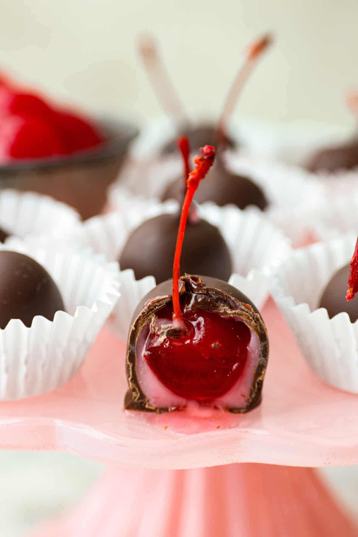 Homemade cherry cordials are a tasty, nostalgic treat! They're made with sweet cherries that are coated in a rich chocolate shell. Make them for Christmas or Valentine’s Day, and watch them disappear! Close up shot of a cherry cordial with a bite taken out of it.