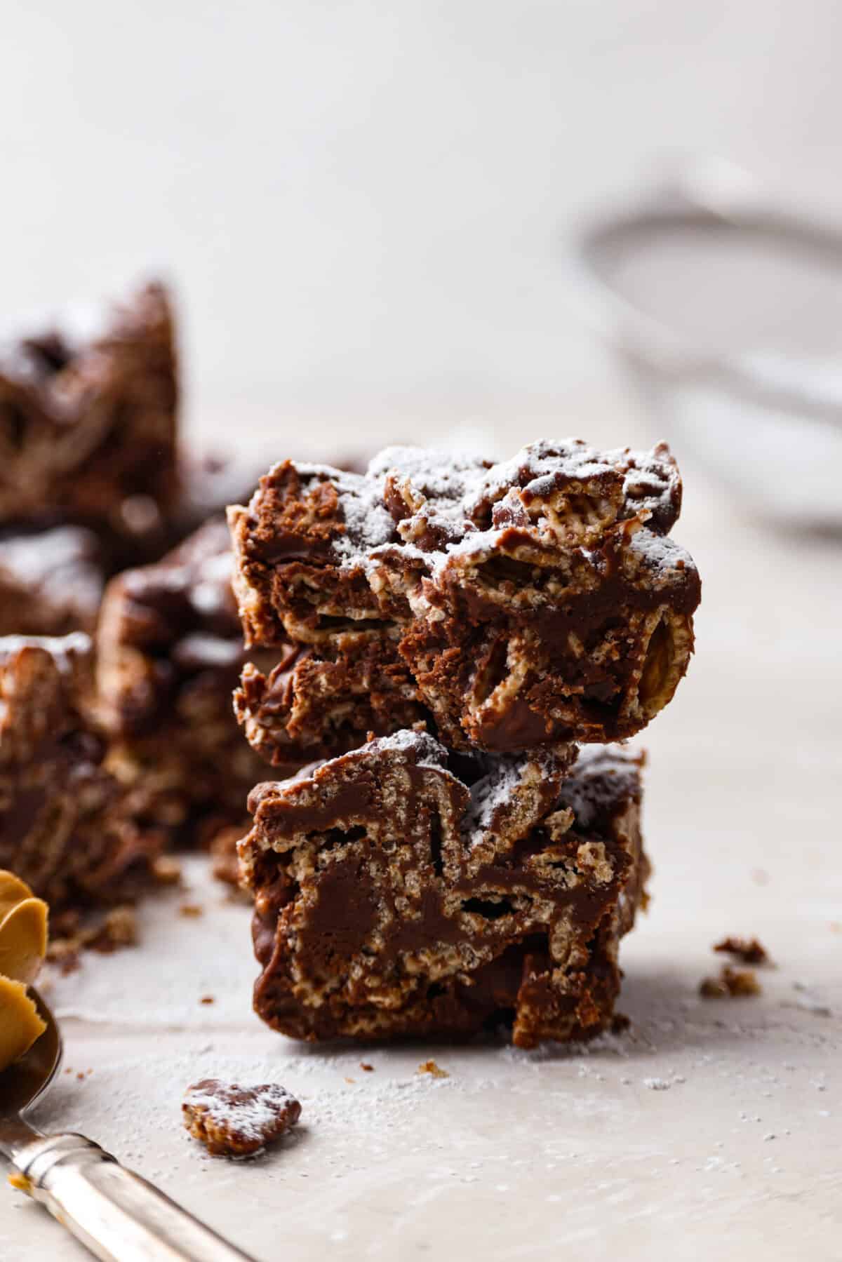 These tasty Muddy Buddy Bars are a fun twist on the classic snack mix. Crunchy cereal is surrounded by sweet marshmallows, chocolate, and peanut butter. These bars are a fun new way to enjoy this classic flavor combination. Side shot of stacked muddy buddy bars.