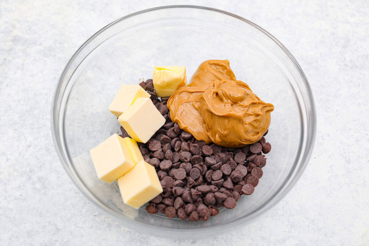 These tasty Muddy Buddy Bars are a fun twist on the classic snack mix. Crunchy cereal is surrounded by sweet marshmallows, chocolate, and peanut butter. These bars are a fun new way to enjoy this classic flavor combination. Overhead shot of butter, chocolate chips and peanut butter in a bowl.
