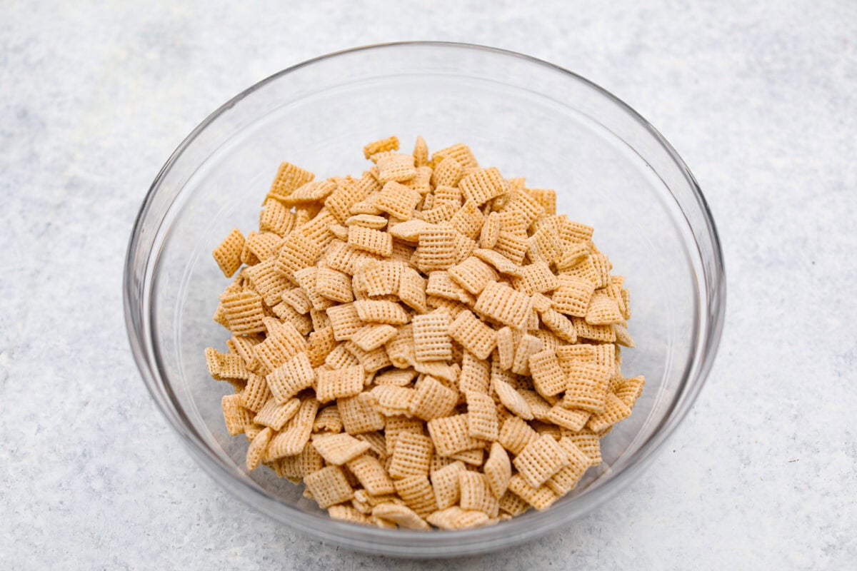 These tasty Muddy Buddy Bars are a fun twist on the classic snack mix. Crunchy cereal is surrounded by sweet marshmallows, chocolate, and peanut butter. These bars are a fun new way to enjoy this classic flavor combination. Overhead shot of cereal in a bowl.
