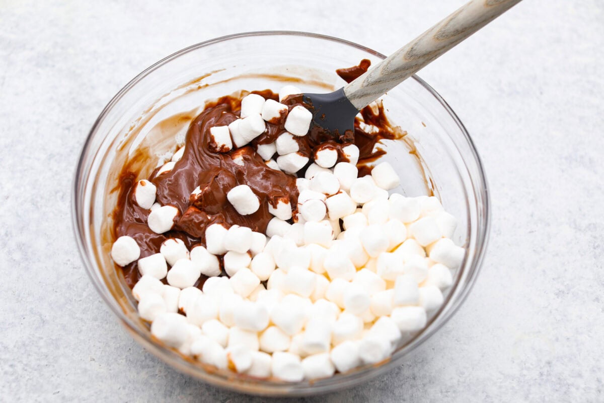 These tasty Muddy Buddy Bars are a fun twist on the classic snack mix. Crunchy cereal is surrounded by sweet marshmallows, chocolate, and peanut butter. These bars are a fun new way to enjoy this classic flavor combination. Overhead shot of mini marshmallows added to the melted peanut butter and chocolate mixture.
