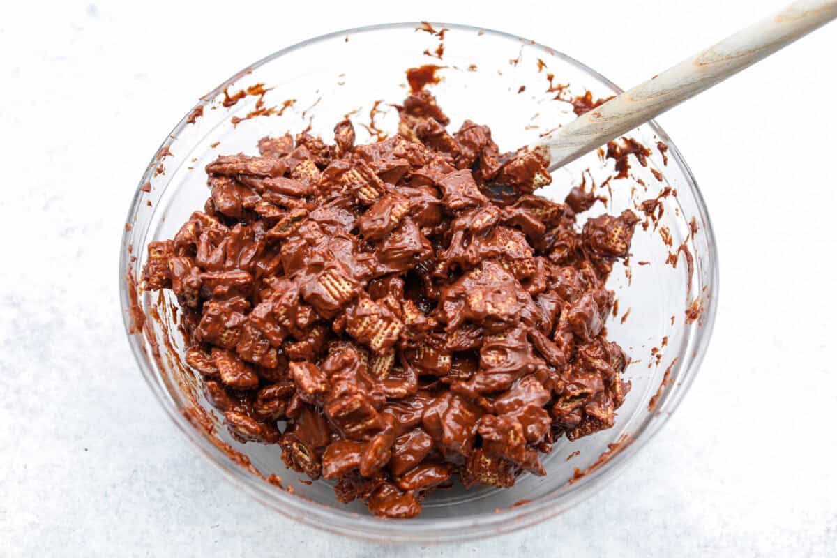 These tasty Muddy Buddy Bars are a fun twist on the classic snack mix. Crunchy cereal is surrounded by sweet marshmallows, chocolate, and peanut butter. These bars are a fun new way to enjoy this classic flavor combination. Overhead shot of the cereal and chocolate marshmallow mixture all mixed together.