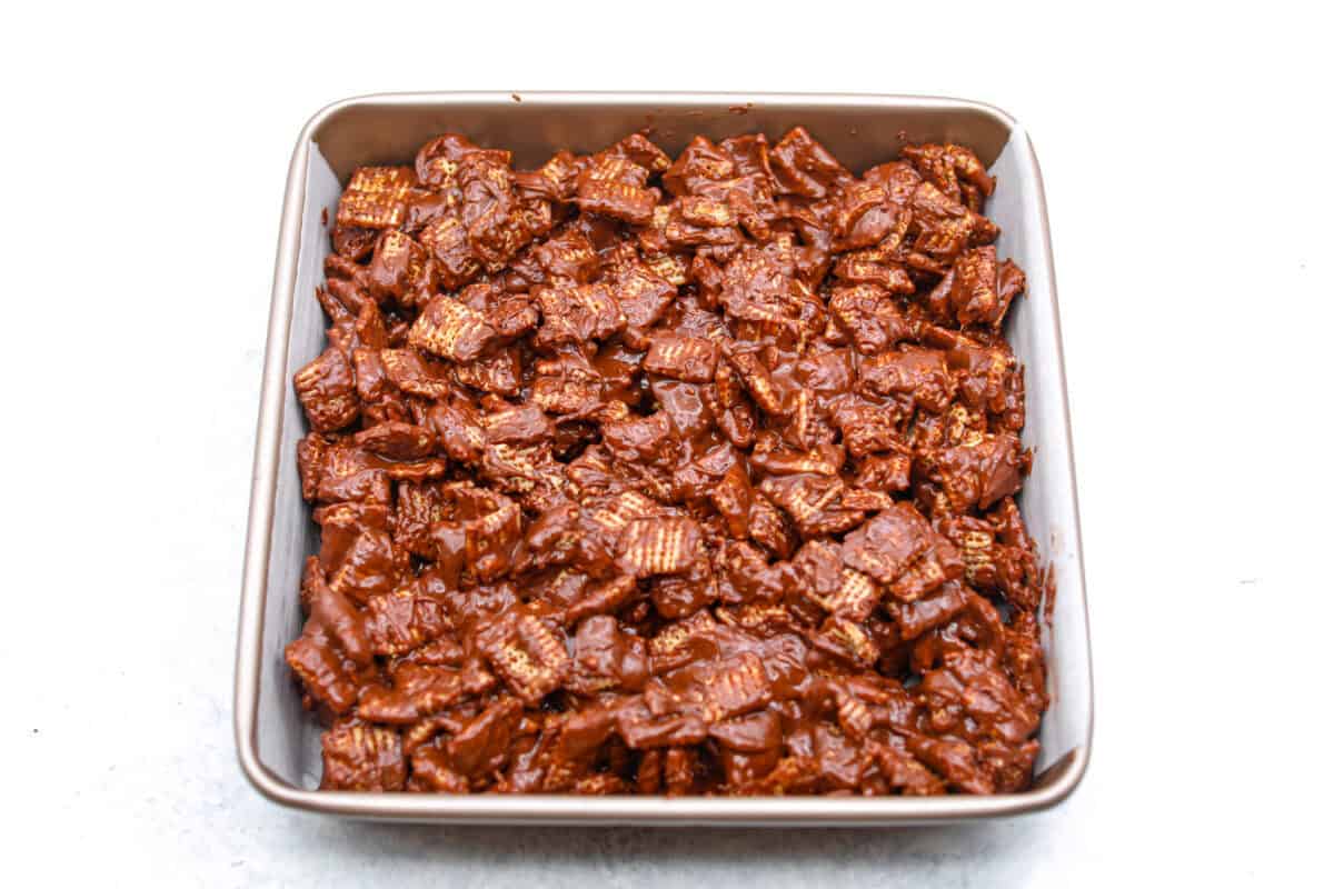 These tasty Muddy Buddy Bars are a fun twist on the classic snack mix. Crunchy cereal is surrounded by sweet marshmallows, chocolate, and peanut butter. These bars are a fun new way to enjoy this classic flavor combination. Overhead shot of muddy buddy bars in a 9x9 pan.