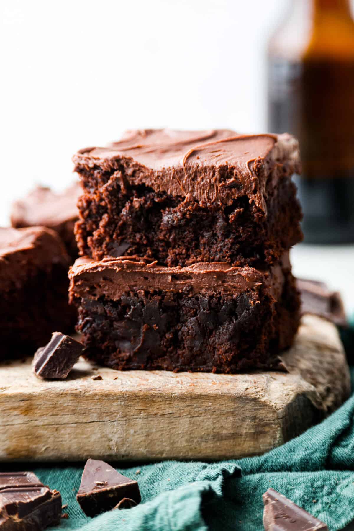 Rich, fudgy, and packed with deep chocolate flavor, Guinness Brownies are a must-try for any dessert lover! The stout beer enhances the cocoa, adding a subtle, malty depth of flavor that makes these brownies rich and irresistibly delicious. Two Guinness brownies stacked on top of each other on top of a wooden board with pieces of chocolate chunks scattered about.